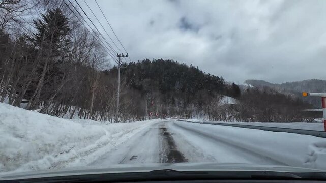 POV dashcam driving on a snowy mountain road in Furano Hokkaido Japan through a winter forest passing under a bridge