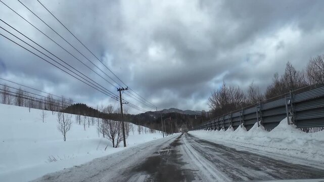 POV dashcam driving on a slushy winter road in Furano Hokkaido Japan with snow fence and mountain view