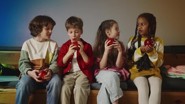 Four happy school friends eating apples during break, healthy school snacks