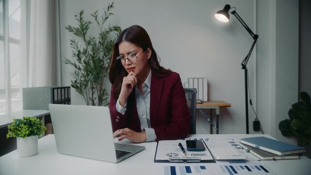 Focused asian businesswoman working on laptop in modern office, analyzing financial data and feeling stressed and tired