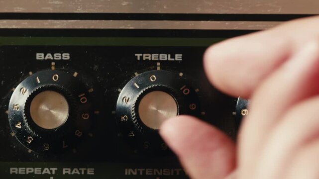 Close-up of plugging a jack into a bass guitar amplifier and turning up the volume knob, live concert show, playing music on guitar tube amplifier.