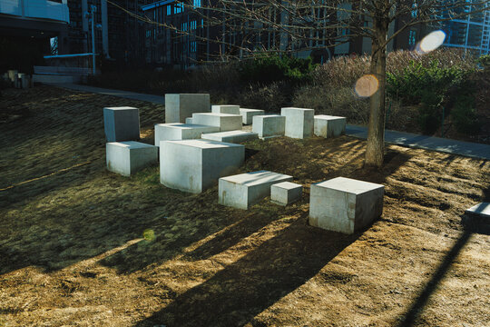 Group of concrete blocks placed on grass with a tree nearby in an urban landscape during daytime showing shadows on the ground