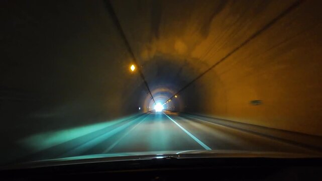 Timelapse POV driving through a highway tunnel with orange lights toward the exit in Tomamu Hokkaido Japan