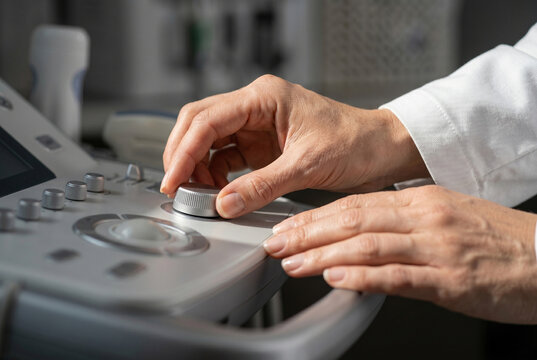 Macro detail of a hand adjusting the control dial on a premium ultrasound machine. The image highlights tactile precision and the micro-topography of high-end medical hardware.

