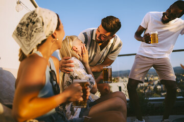 Obraz premium Happy diverse friends enjoying beer at rooftop party
