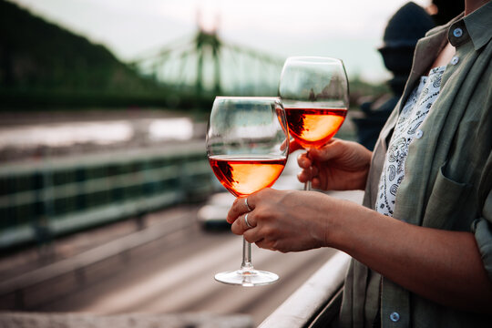 Hand holding glasses of rose wine in summer sunshine during a outdoors party or a picnic.