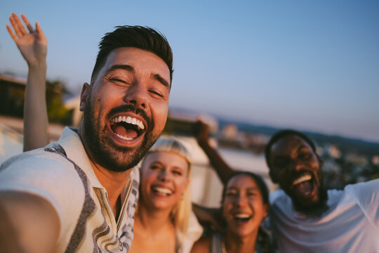Diverse friends taking selfie laughing on rooftop during sunset