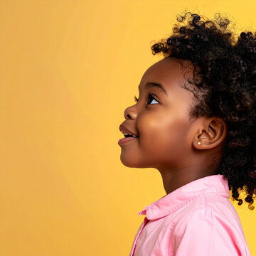 Retrato de ni&ntilde;a peque&ntilde;a sonriendo y mirando hacia arriba sobre fondo amarillo con expresi&oacute;n alegre, concepto de infancia feliz, familia, educaci&oacute;n, salud o marcas infantiles con espacio para texto