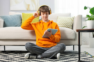 Obraz premium Teenage boy in headphones using tablet on floor at home