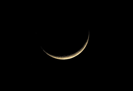 A sharp waxing crescent moon hangs in the pitch-black night sky. This high-contrast shot reveals the rugged texture of craters along the lunar edge, glowing with a soft, warm golden light.