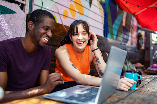 Young adults collaborating on laptop at outdoor cafe