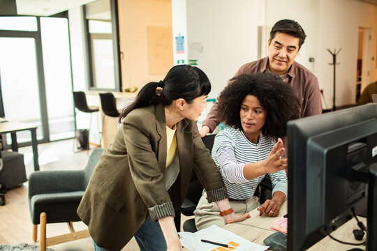 Coworkers collaborating at computer in modern open plan office