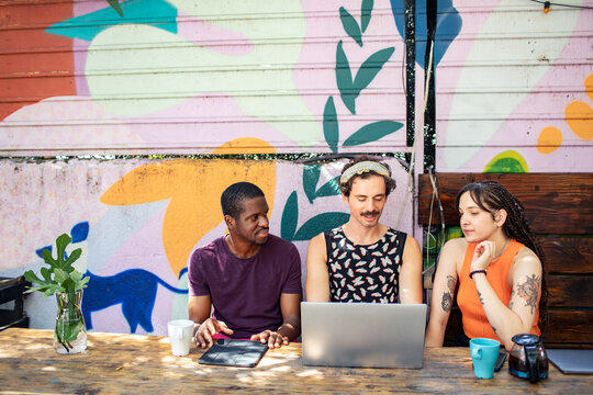 Three friends coworking with laptop and tablet at colorful outdoor cafe