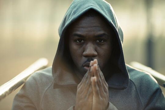 Focused young man in hoodie with praying hands outdoors
