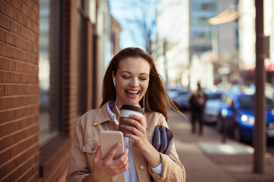 Smiling woman with coffee using smartphone on city sidewalk