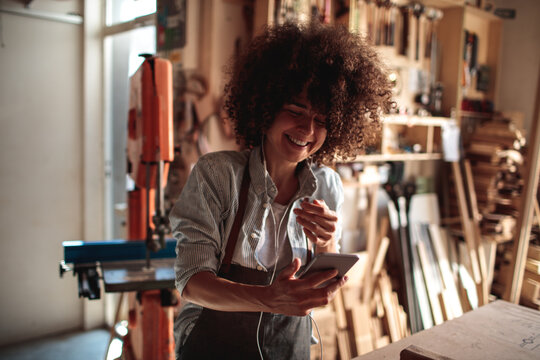 Smiling woman using smartphone in woodworking shop