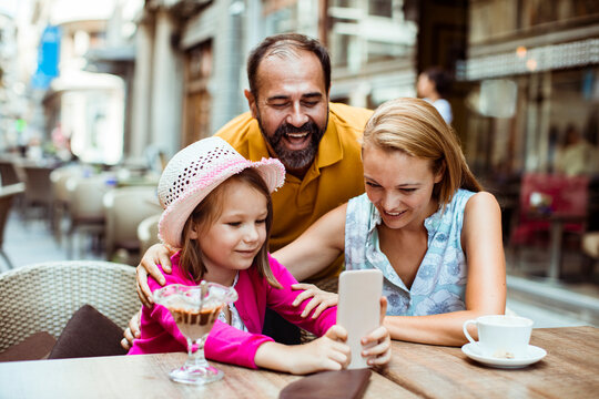 Happy family using smartphone at outdoor street cafe
