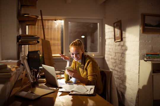 Smiling young woman video calling while working at home office at night