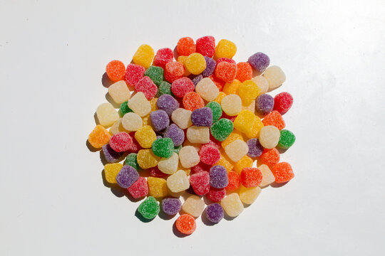 Colorful gumdrops are piled together on a white background each piece coated with sugar creating a bright playful pattern with varied shapes and vibrant candy colors