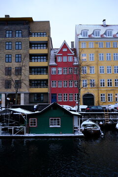 Winter waterfront at Christianshavn, Copenhagen, with snow-covered rooftops and yellow and red house facades reflected in calm canal water.