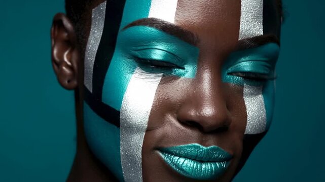 Makeup artist applies paint in bright colors on a model's face in a studio. The model poses with different expressions, showcasing the artwork in close-up shots.