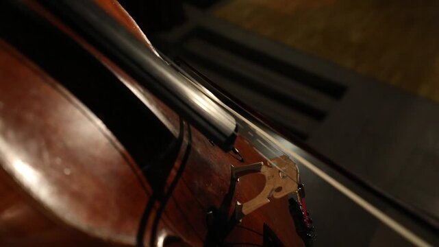 Close up of a talented musician playing the cello. The bow moves across the strings, creating classical music. Warm lighting highlights details of the beautiful wooden acoustic instrument.

