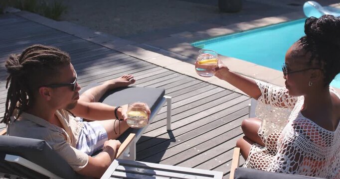 African American couple clinking glasses after woman lifting glass, celebrating on poolside deck
