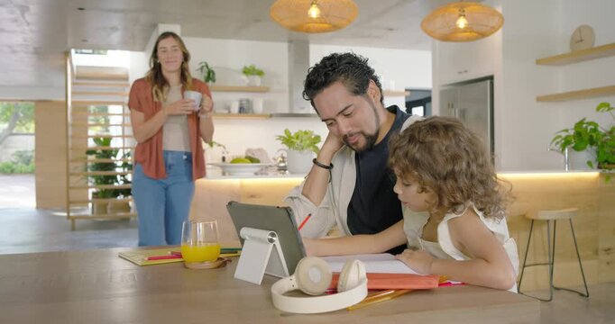 Diverse parents guiding child for homework on tablet at table in kitchen while mother placing mug