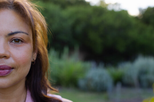 African American woman posing outdoors in garden, showing hoop earring and pink blouse, copy space