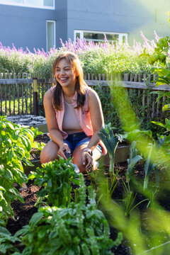 African American woman kneeling tending raised beds in home garden with tool, wearing denim shorts