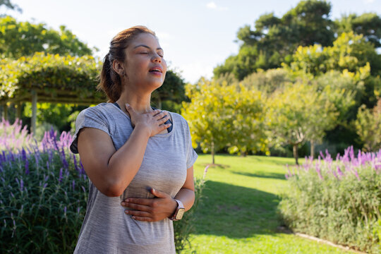 African American woman standing in park breathing with watch and sensor on gray athletic shirt