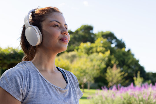 African American woman standing listening at park, tee, black sports-bra strap, headset, copy space