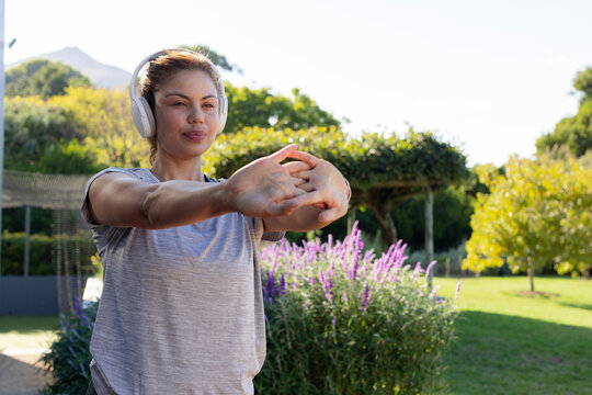 African American woman stretching arms in garden near purple flowers wearing grey tee headphones