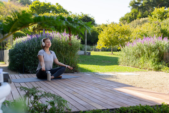 African American woman sitting cross-legged on yoga mat on wooden deck, meditating with headphones