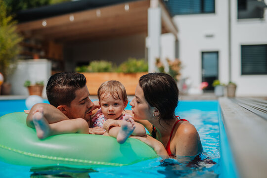 Parents and child having fun with floatie in garden swimming pool