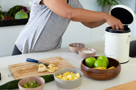 African American woman leaning over kitchen counter putting fruit scraps into COMPOST bin