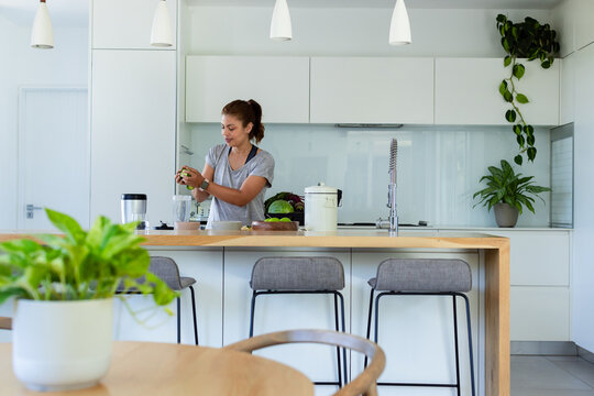 African American woman preparing fruit on wooden island in kitchen with blender, wearing grey tee