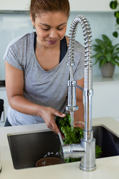 African American woman rinsing leafy greens under spring faucet at kitchen sink wearing gray tee
