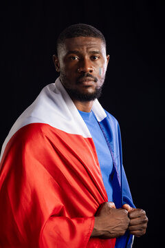 Mid adult African man posing in studio with black backdrop, blue shirt, tricolor cloth, face paint