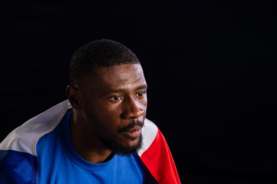 Mid adult African man leaning forward, gazing right in blue tee with red-and-white flag, copy space