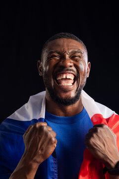 Mid adult African man shouting, gripping tricolor flag, wearing blue shirt and face paint in studio
