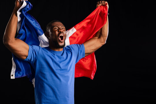 Man shouting while holding large tricolor flag behind shoulders, wearing blue shirt in studio