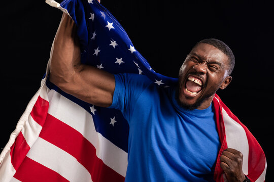 African American man flexing and shouting in blue tee while draping United States flag in studio