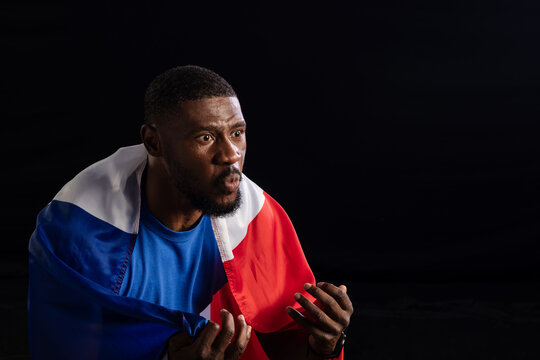 African man gesturing and looking right in studio, wearing blue shirt, draped in flag, copy space