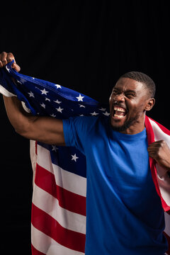 Man cheering and draping United States flag across shoulders in studio wearing blue tee