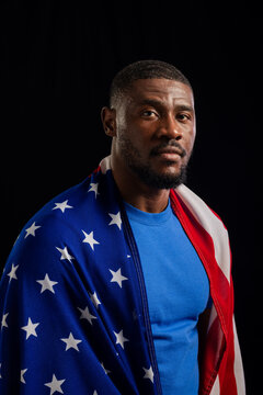 African American man standing, wearing American flag and blue crew-neck shirt in studio