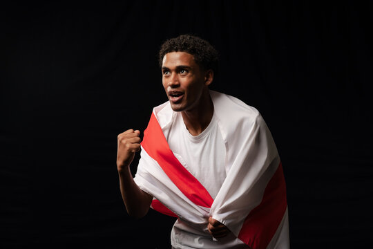Adult man of African descent leaning, gripping white-and-red flag, wearing white t-shirt in studio