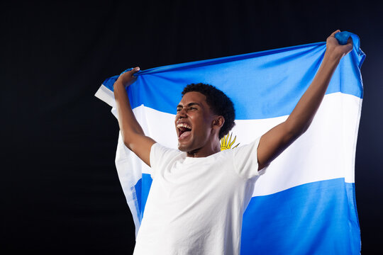 African man cheering, holding blue white flag with golden sun in studio wearing white T-shirt