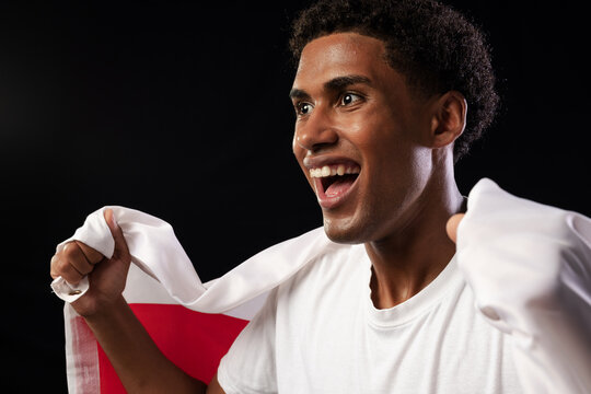 Man in 20s wearing white T-shirt gripping red-and-white flag with ringed hand in studio