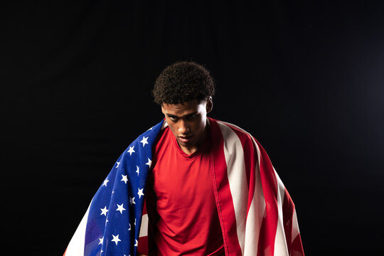 African American man in his 20s wearing red athletic shirt and draping US flag in studio
